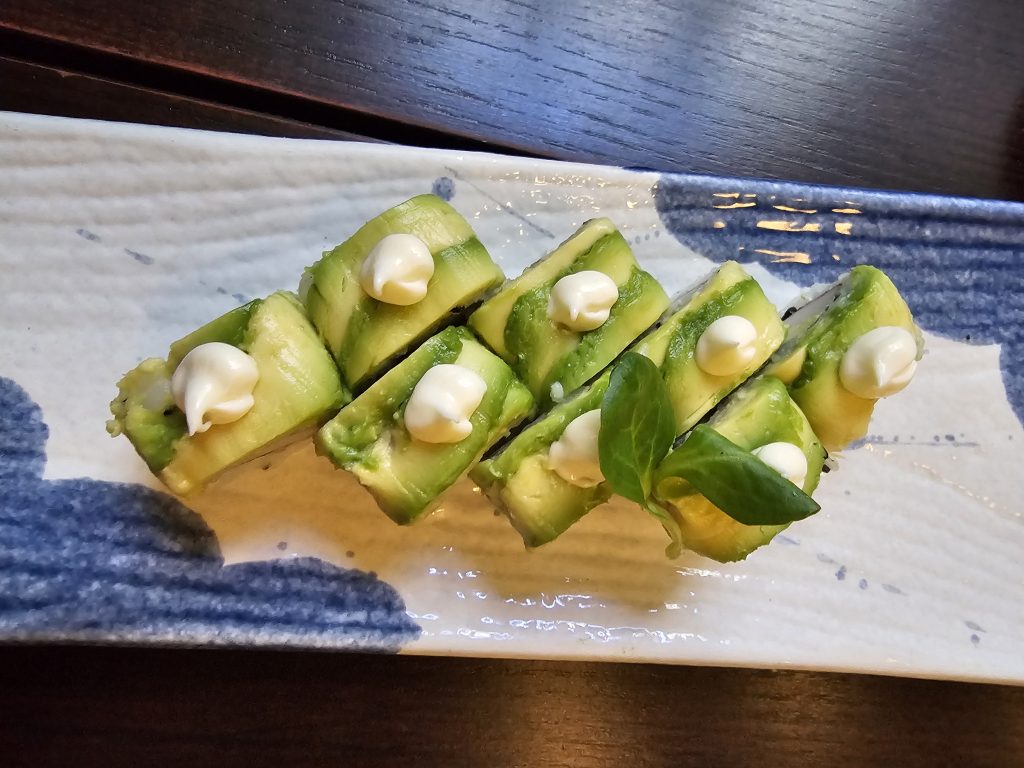 Avocado-topped vegetarian sushi rolls with little dots of mayo on a blue and white plate